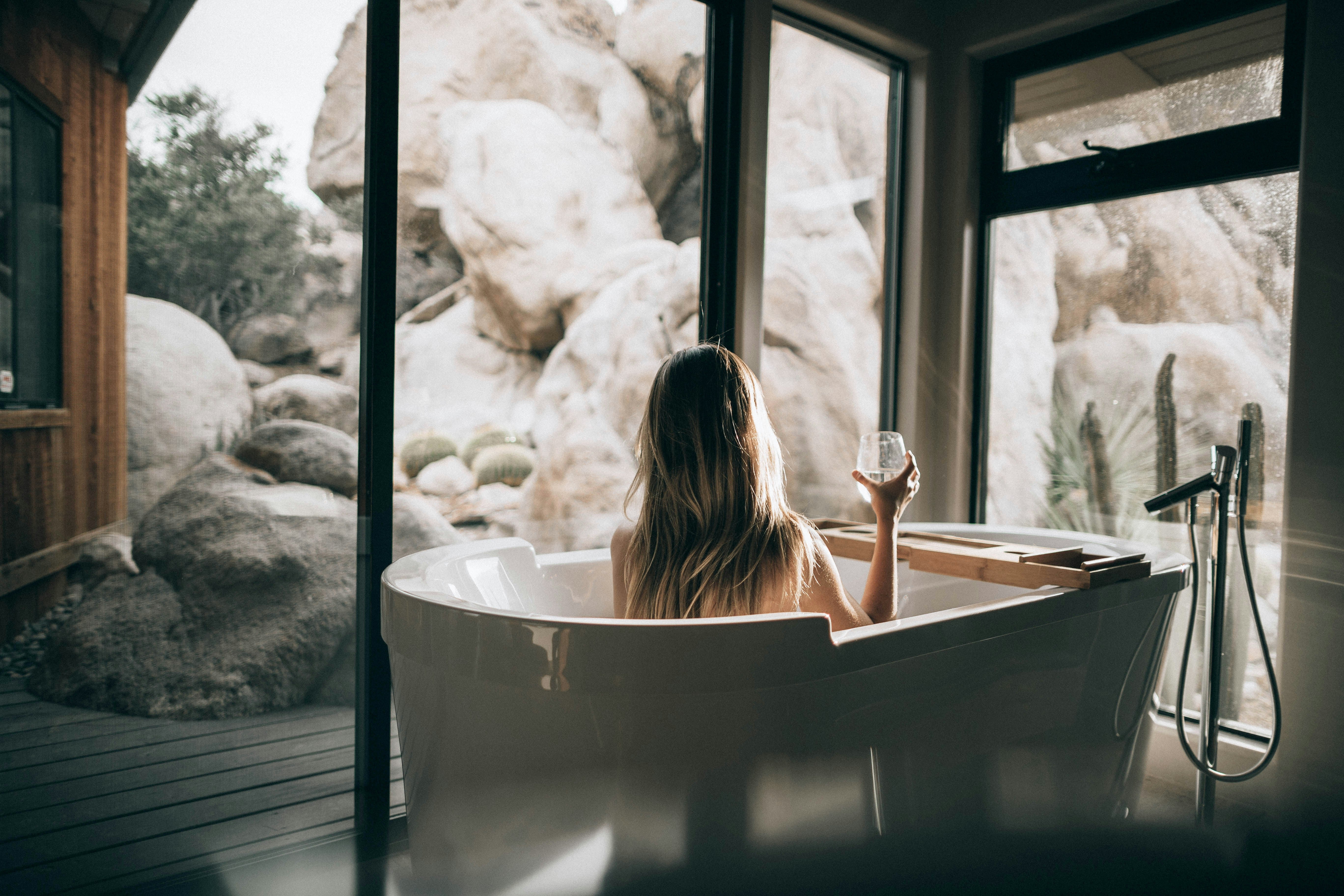 Woman drinking a glass of white wine in a bath tub