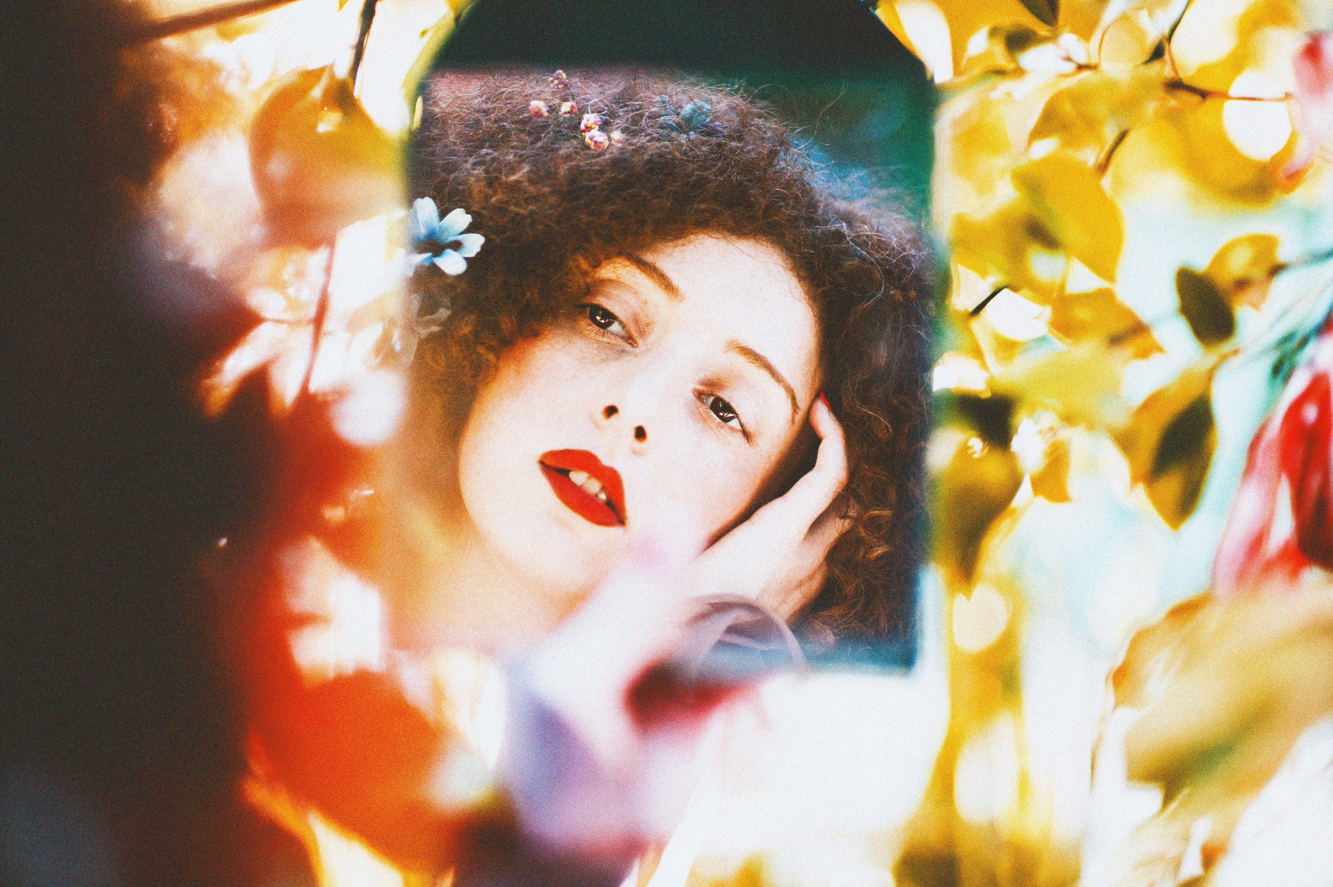 Woman looking at herself in a mirror, surrounded by flowers